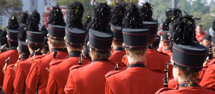 Marching band in red and black uniforms photographed from behind before game