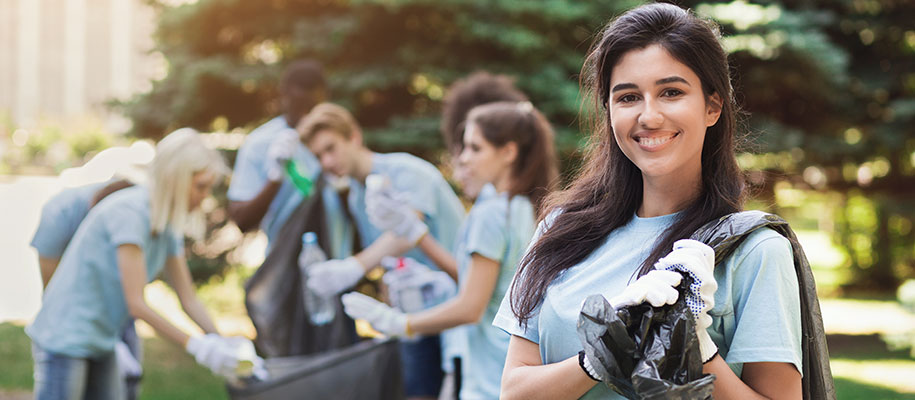 Young White female with group of volunteers holding garbage bags cleaning park