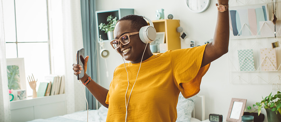 Black woman dancing around dorm with over-the-head headphones on