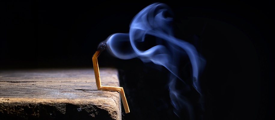 Burnt out matchstick bent to look like it's sitting on table edge in dark