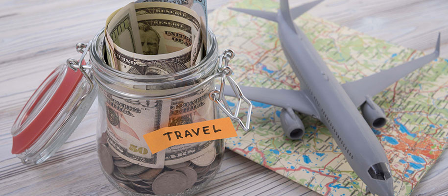 Toy plane on folded map and full money jar with sign reading Travel