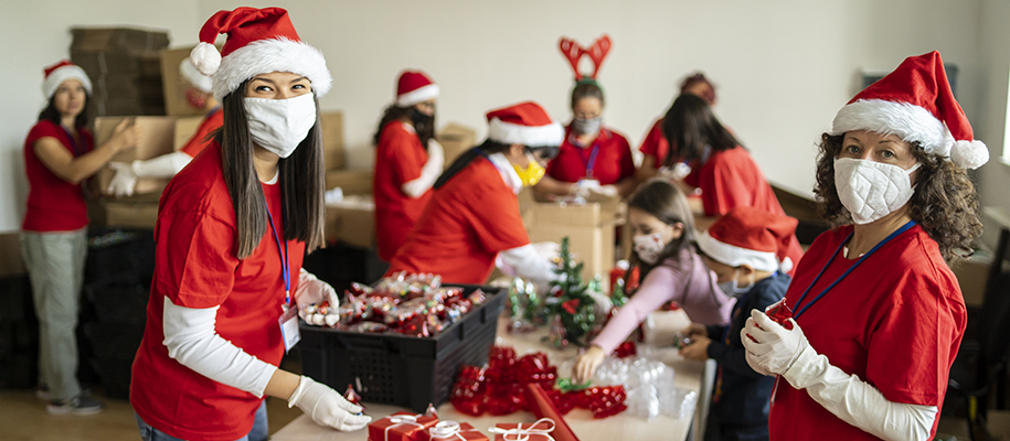 Group of volunteers in red, Santa hats, and face masks packing donation gifts