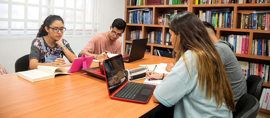Four Hispanic students in library at table with laptops and notebooks