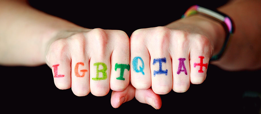 Hands of white person with LGBTQIA+ written on knuckles in rainbow colors