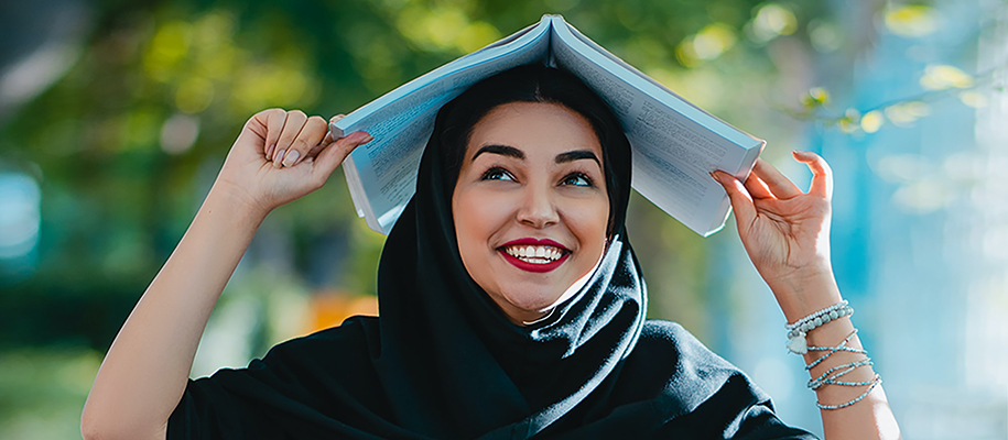 Woman in black Al-Amira with red lipstick on and book open on top of head