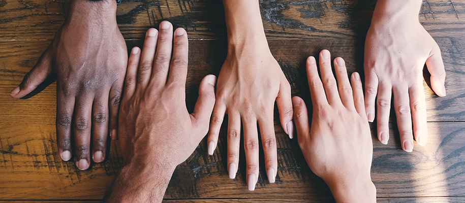 Hands of people of various races and genders resting beside one another on wood