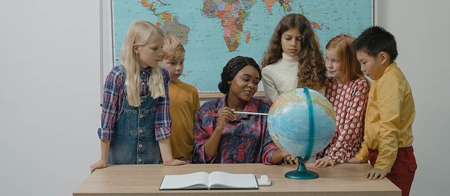 Black teacher showing group of children countries on a globe seated at a desk