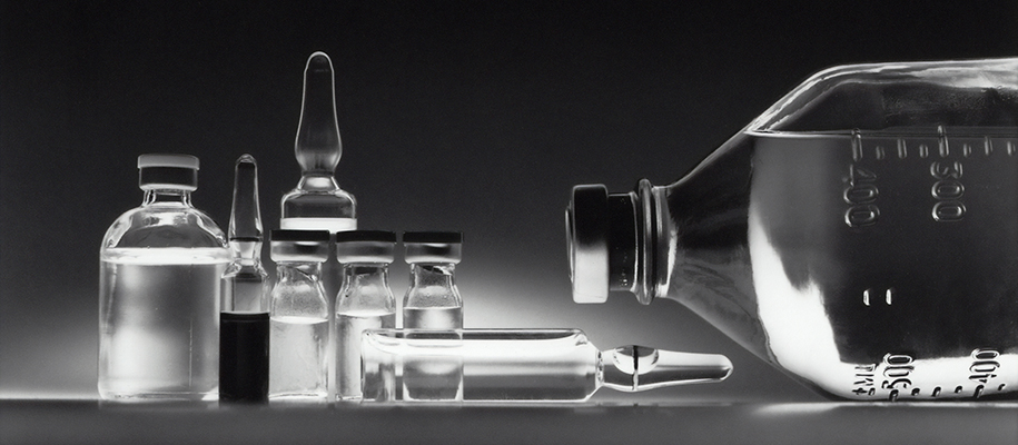 Various vials and glass containers filled with clear medical liquid, backlight i