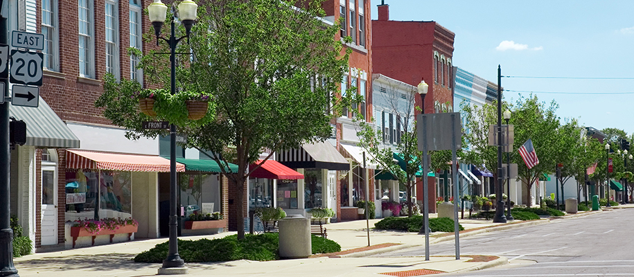 Small-town shopping street with brick buildings, colorful awnings during day