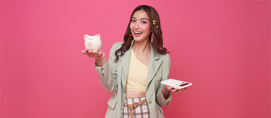 Young Asian woman in trendy outfit, clips in hair holding piggy bank, calulator