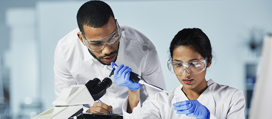 Black man with clipboard and Middle Eastern woman doing experiments in lab coats