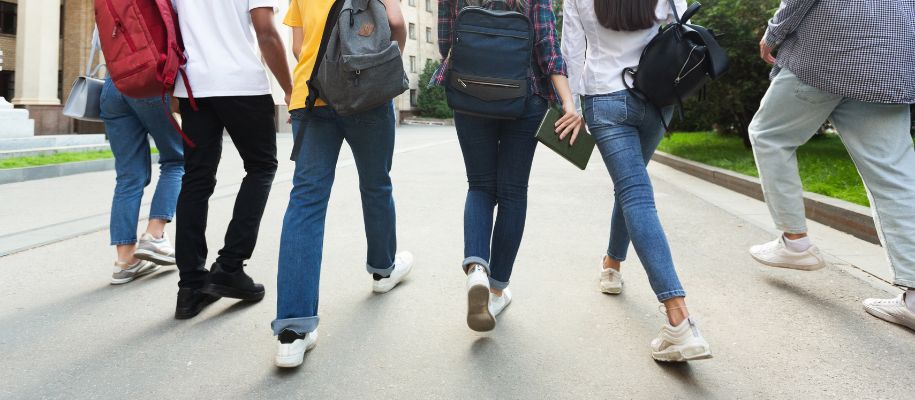 Legs of group of students with backpacks walking down campus road