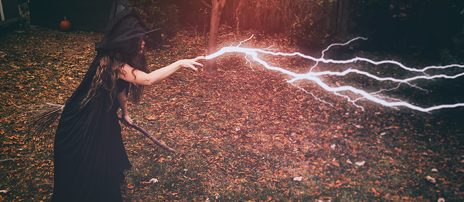 White witch in black hat and dress holding broom and ejecting lightening from fingers