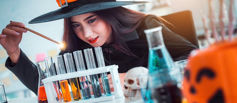 Asian witch with wand doing magic on beakers of liquid in science lab