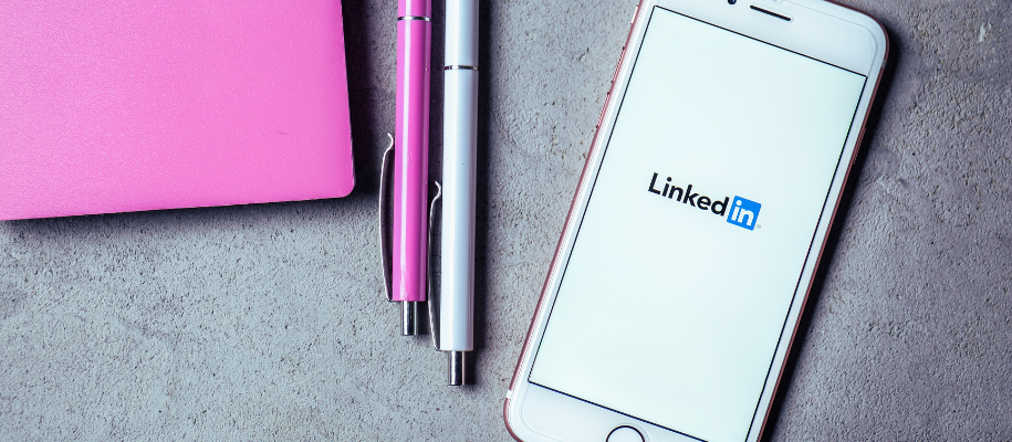 Phone with LinkedIn logo next to white and pink pens and pink notebook