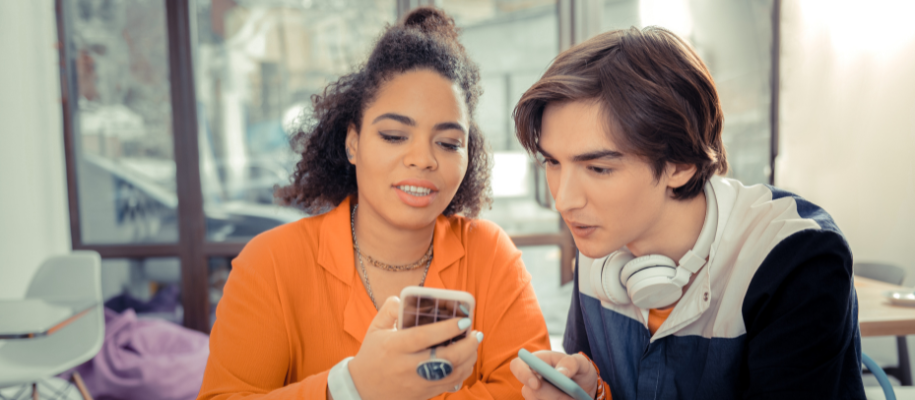 Diverse young man and woman looking at phones together in coffee shop