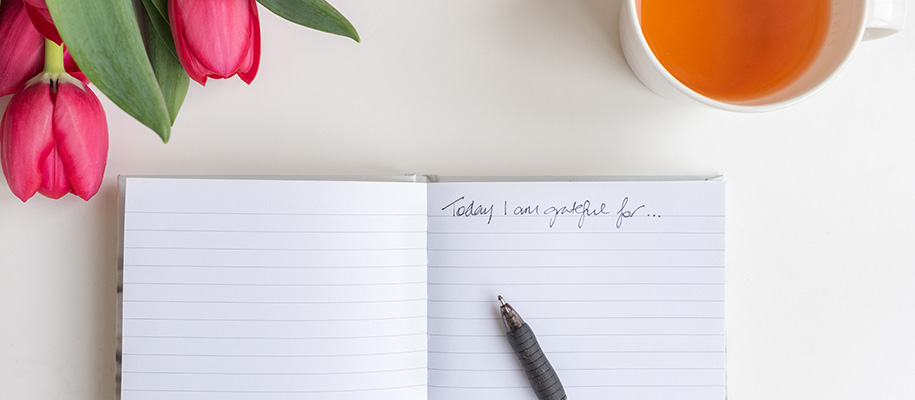 Notebook open to Today I am grateful, pen resting on top, tulips and tea