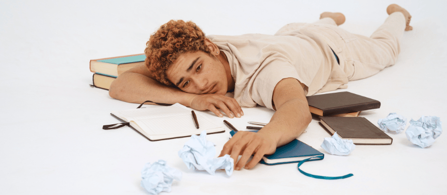 Student laying on floor surrounded by crumpled paper and notebooks