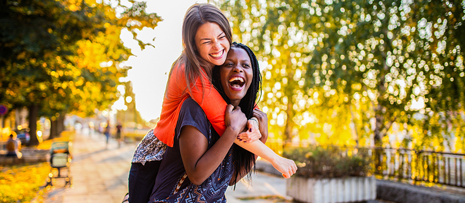 Two friends joyously laughing and smiling, woman on other woman's back