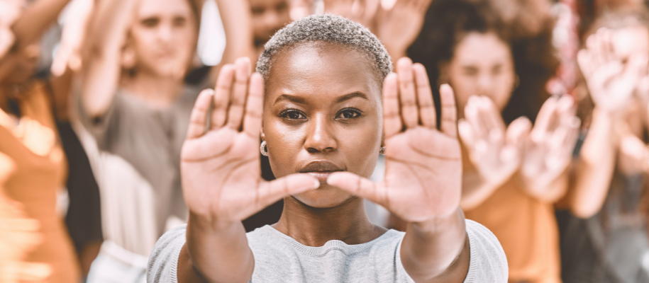 Black woman with short hair holds hands up in stop gesture, crowd blurred behind