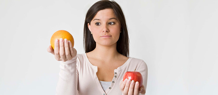 Young White female holding and comparing an orange and apple in each hand