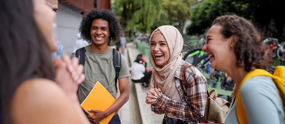 Group of diverse students outside laughing, focus on woman in hijab
