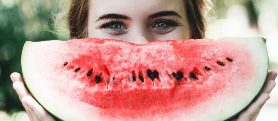 Brunette female teen holding pink seeded watermelon wedge to mouth like a smile