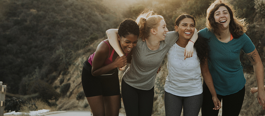 Four diverse female friends in workout clothes, laughing on a hike