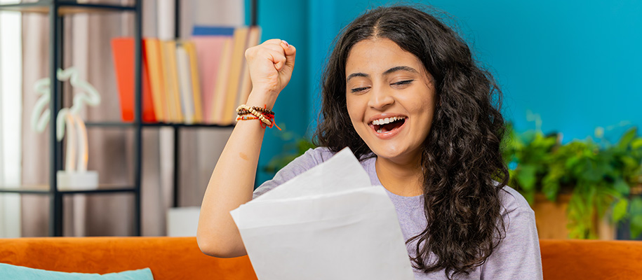 Indian girl with fist in air, smiling in excitement, looking at opened mail