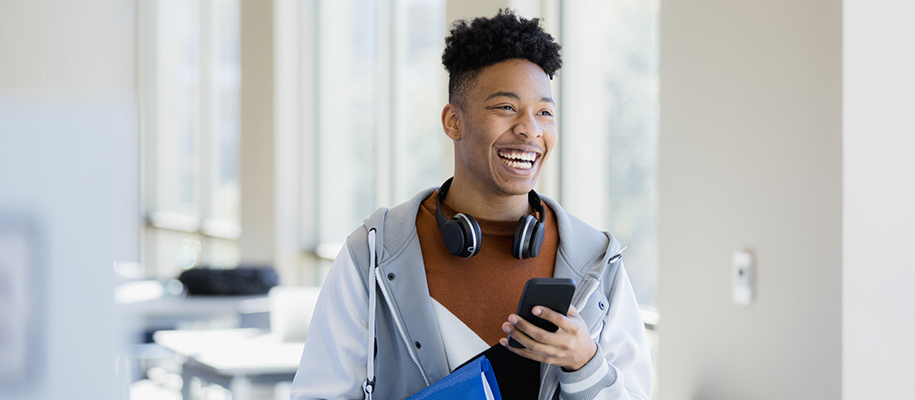 Smiling Black male with headphone around neck phone in hand, in grey jacket