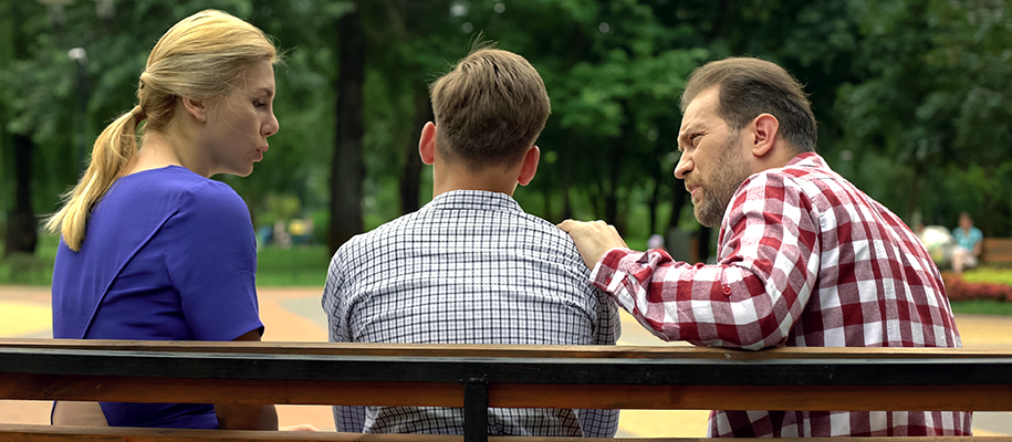 Back of blond mom and dad in plaid sitting on bench, comforting son in plaid