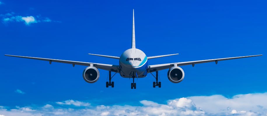 Blue and white airplane with wheels down flying toward camera on bright blue sky
