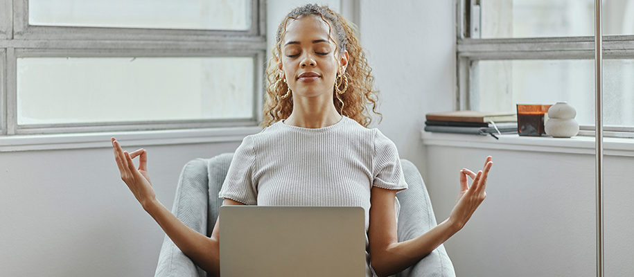 Multiracial woman with long curly hair, big earrings, meditating with laptop