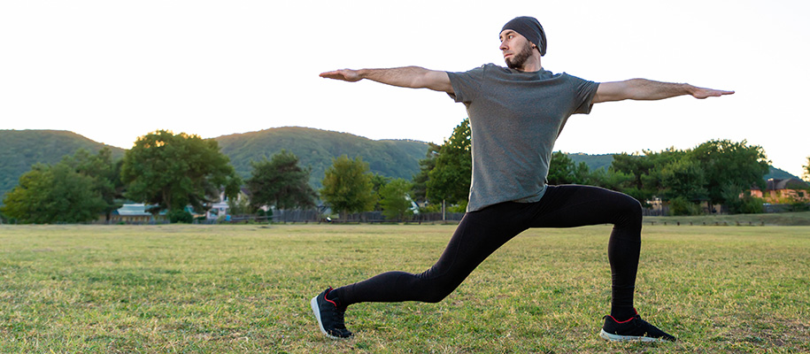 White man with beard in workout gear and beanie doing yoga outside