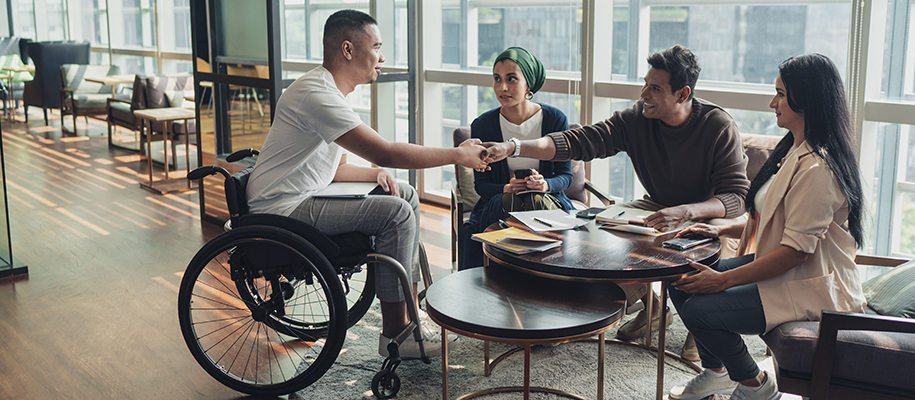 Four diverse people meeting at table, Asian man in wheelchair shaking hands