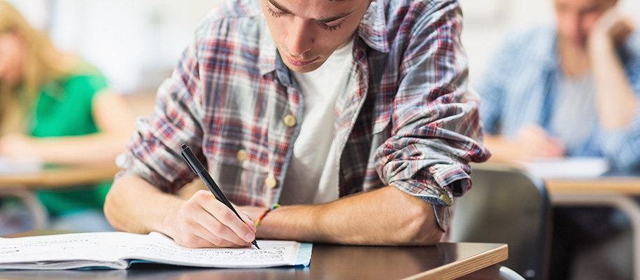 White young man in plaid at desk writing notes in notebook