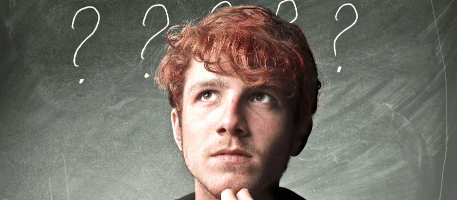 Young man with questioning expression. Question marks behind him on chalkboard.