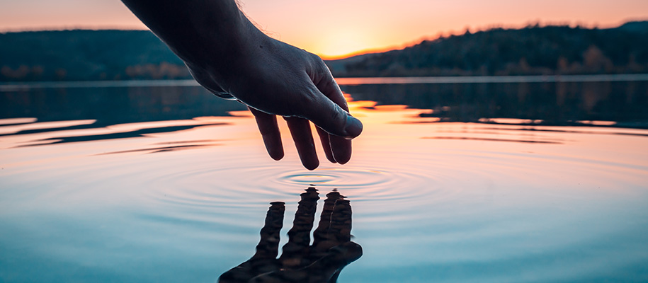 Hand of White man rippling lake surface with fingers, reflection in water