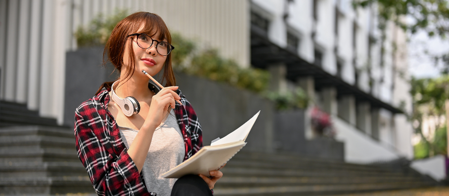 Asian women student in plaid shirt with headphone writing in notebook outside