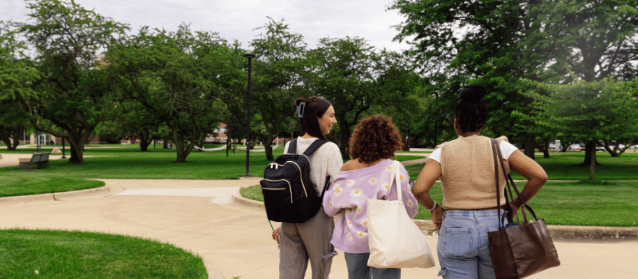 Three student are seen from the back looking at a crossroads on a campus green