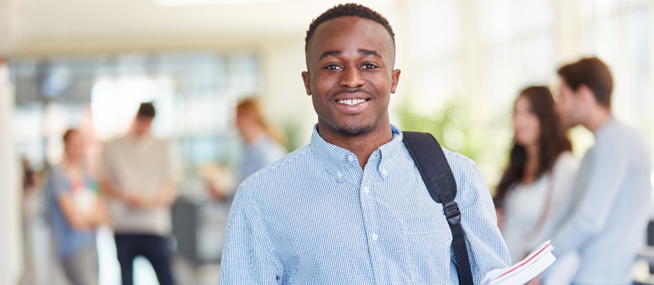 Black male student in blue dress shirt smiling at camera, other students behind