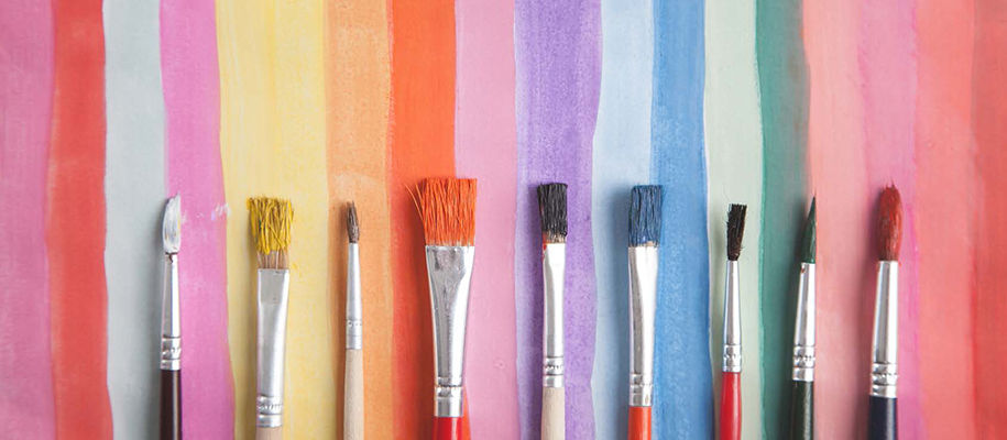 Line of paint brushes covered in paint on rainbow painted piece of paper