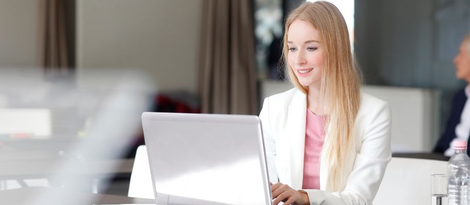 Young White blond women in white blazer and pink shirt at laptop in office