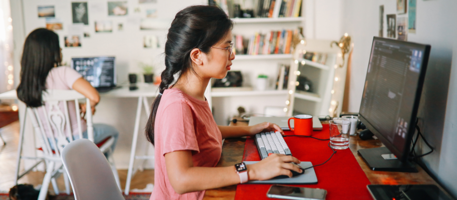 Young Asian woman in pink shirt at desk with red desktop, computer in bedroom