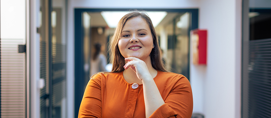Confident plus-sized woman in orange shirt, hand under chin, in office hallway