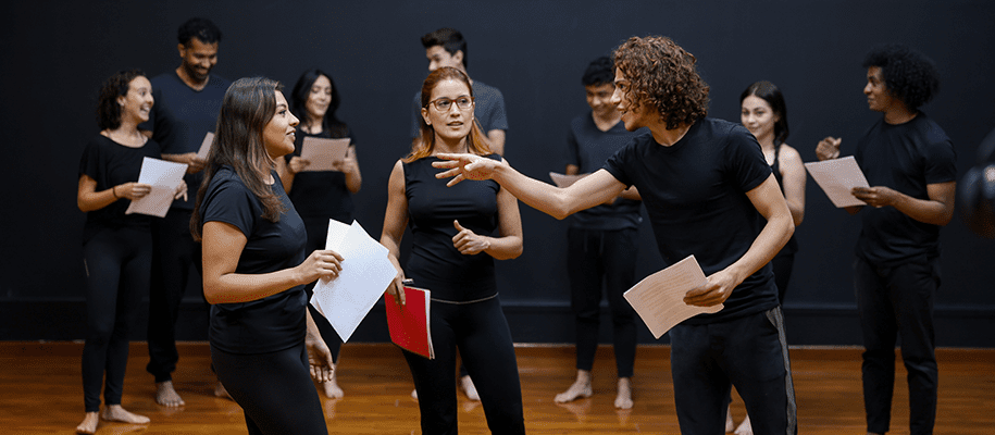 Students wearing black in acting class, two actors working on scene with teacher