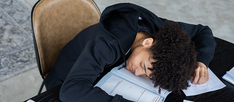 Curly-haired Black student napping on books and papers at desk for studying