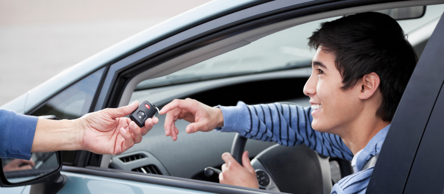 Young Asian man in blue striped sweater in car reaching for key in peron's hand