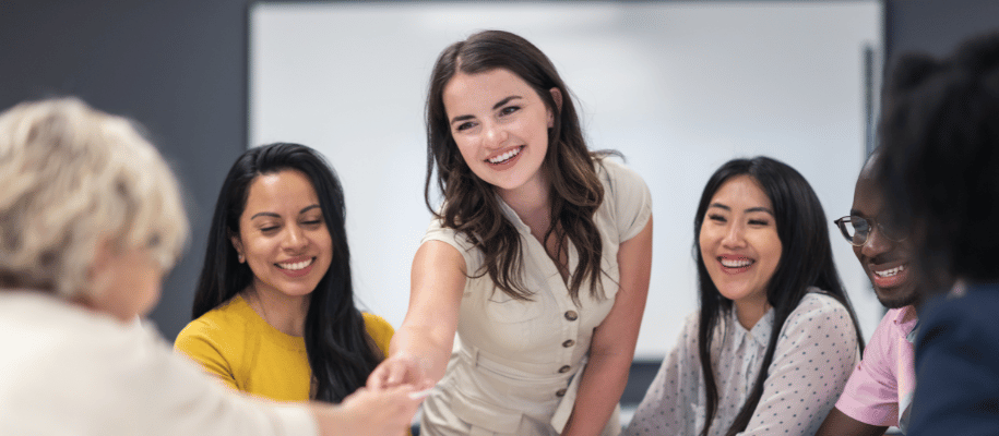 Female student stands over a table reaching for a note from other student
