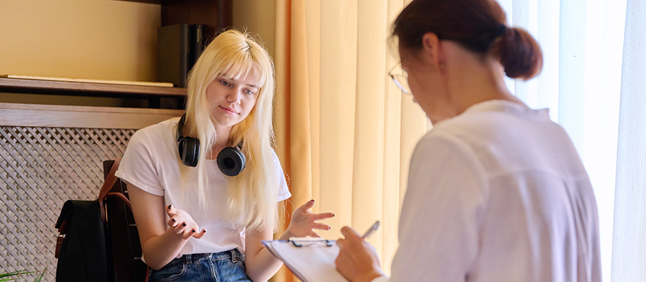 White blond young woman, headphones around neck, talking to counselor